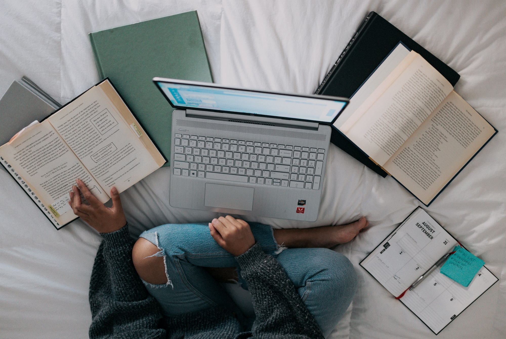 Woman sitting on her bed, surrounded by University text books and laptops. 6 things to do after University.
