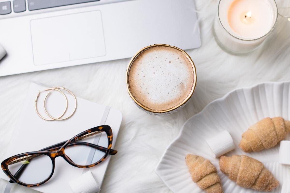 Flat lay of a laptop, coffee, glasses, snacks and a candle. This Splendid Shambles.