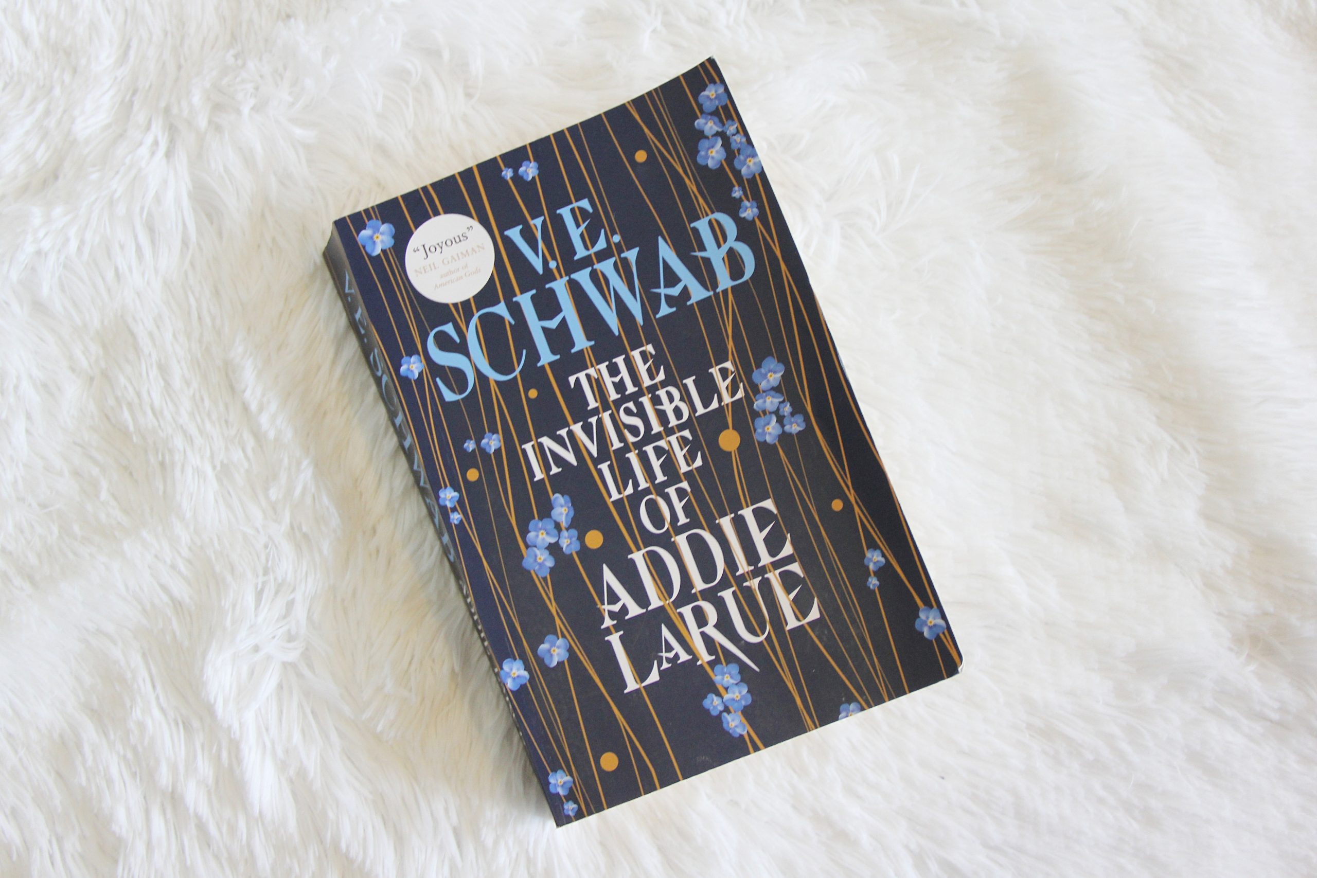 The Invisible Life of Addie LaRue by VE Schwab on a fluff white blanket.