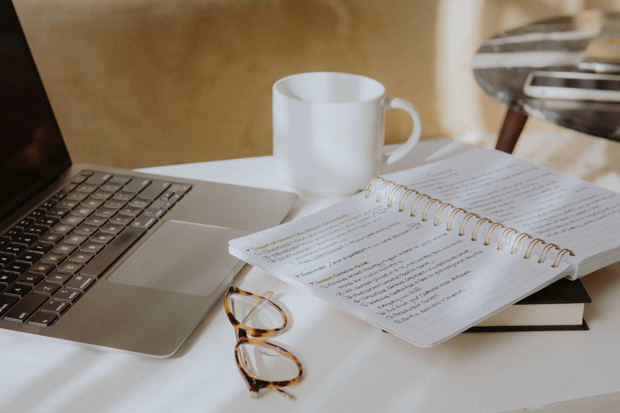 Laptop, mug, notebook and glasses on a desk - how to write productivity at home and avoid burnout