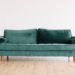 Green velvet loveseat sofa in front of a white wall, on wooden floor. The best fabrics for furniture reupholstery on This Splendid Shambles