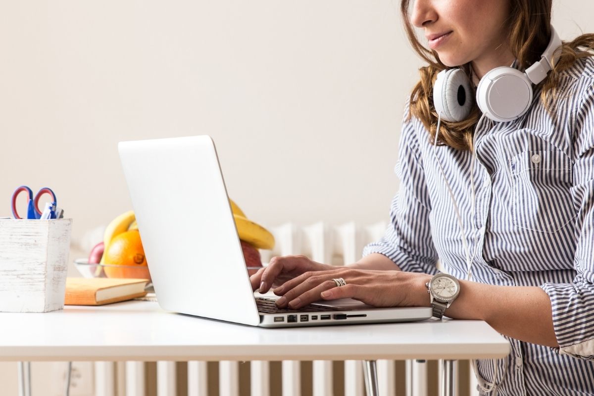 Woman in a blue shirt and headphones around her neck, sitting a table with her fingers on laptop keyboard. Is blogging still relevant? Blogging tips on This Splendid Shambles.