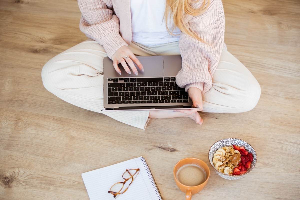 Woman in a pink cardigan and white pants sitting on the floor with a laptop on her lap. 6 tips on content creation for social media on This Splendid Shambles.