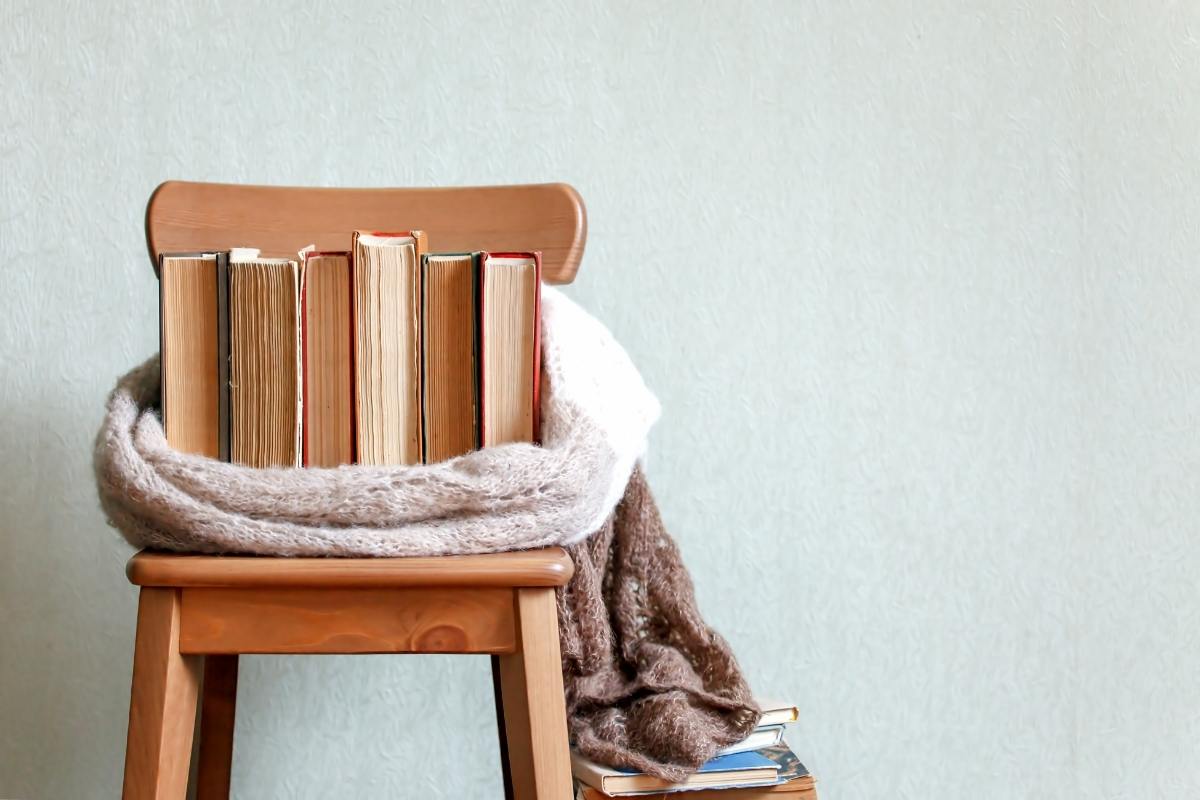 A selection of books sitting wrapped in a blanket, sitting on a wooden chair.