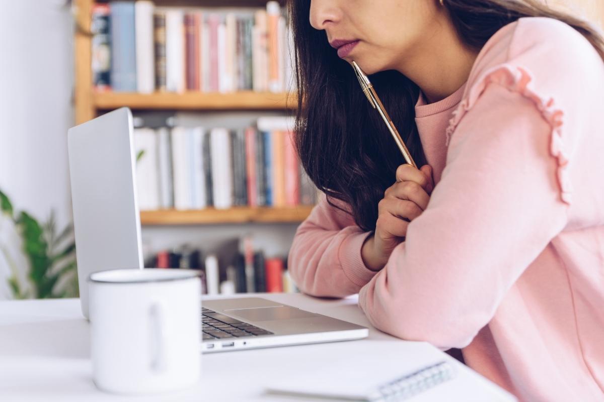 Woman in a pink sweater, holding a pen to her lip while leaning on a desk with a laptop on it. 5 Rules for writing your first guest blog post - This Splendid Shambles