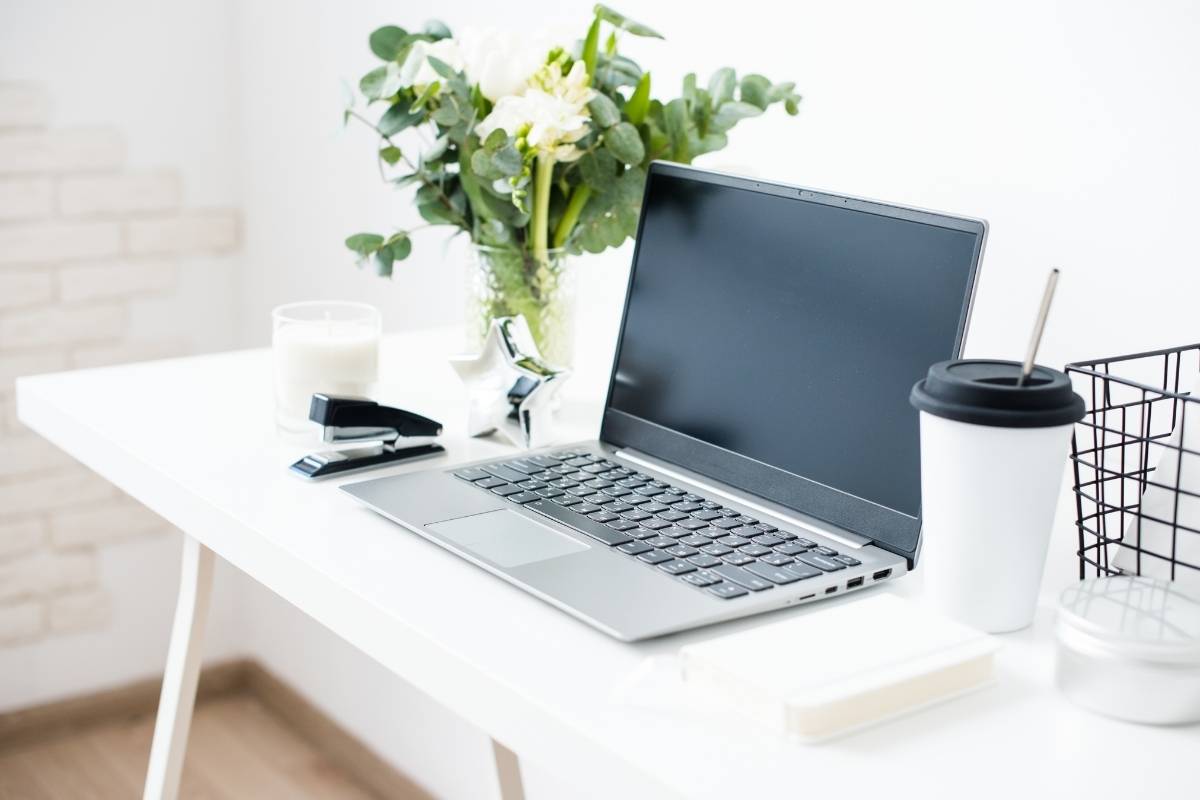 Laptop sitting on a white desk. Coffee in the right foreground, plant in the background. Blogging For small Business - This Splendid Shambles