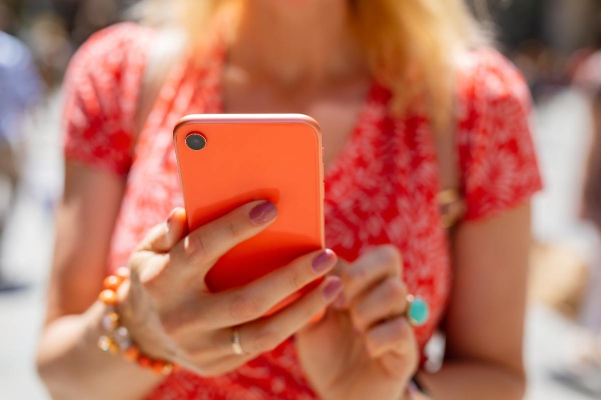 Close up of a woman holding a phone with an orange cover. She's wearing a red dress, and has pink finger nails.
