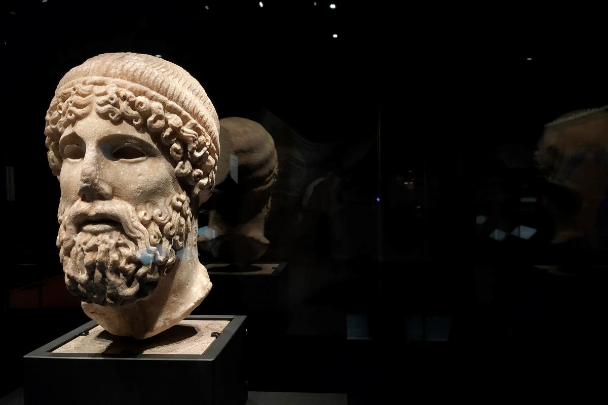Black background with a Greek stone head to the left.