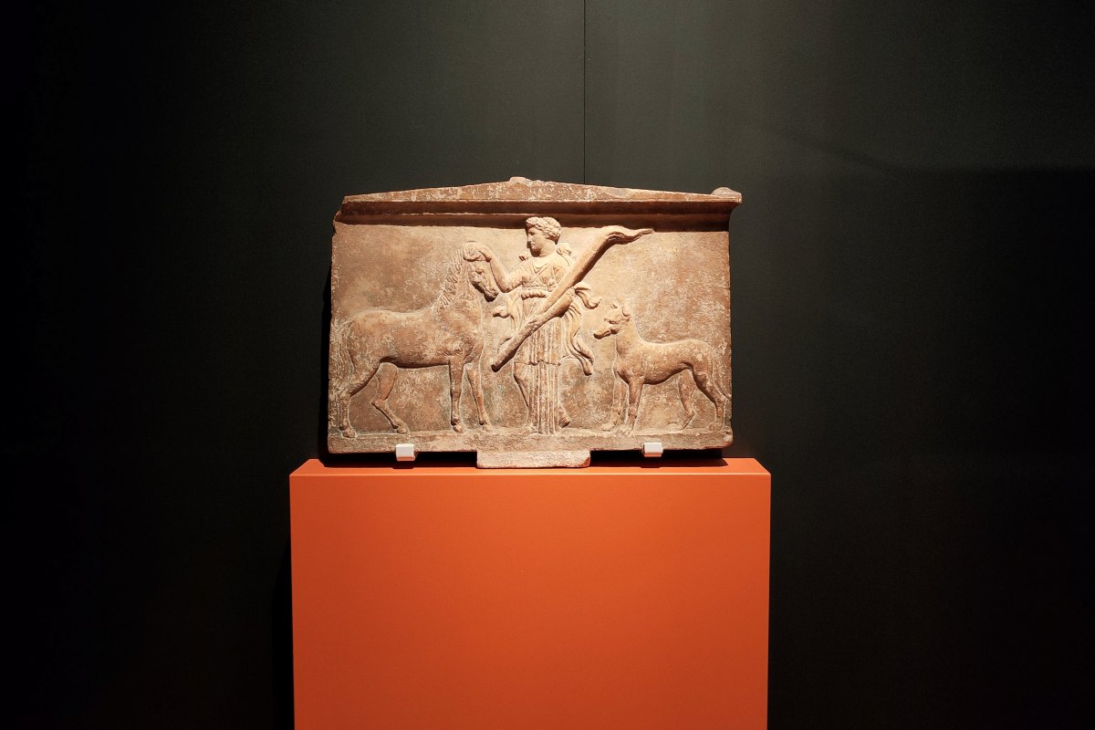Black background with a piece of Ancient Greek temple frieze on an orange plinth.