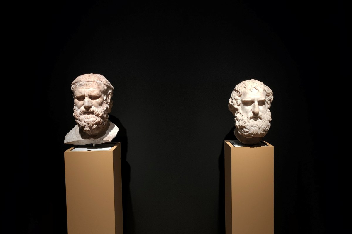 Black background with 2 Greek statue heads on light brown plinths.