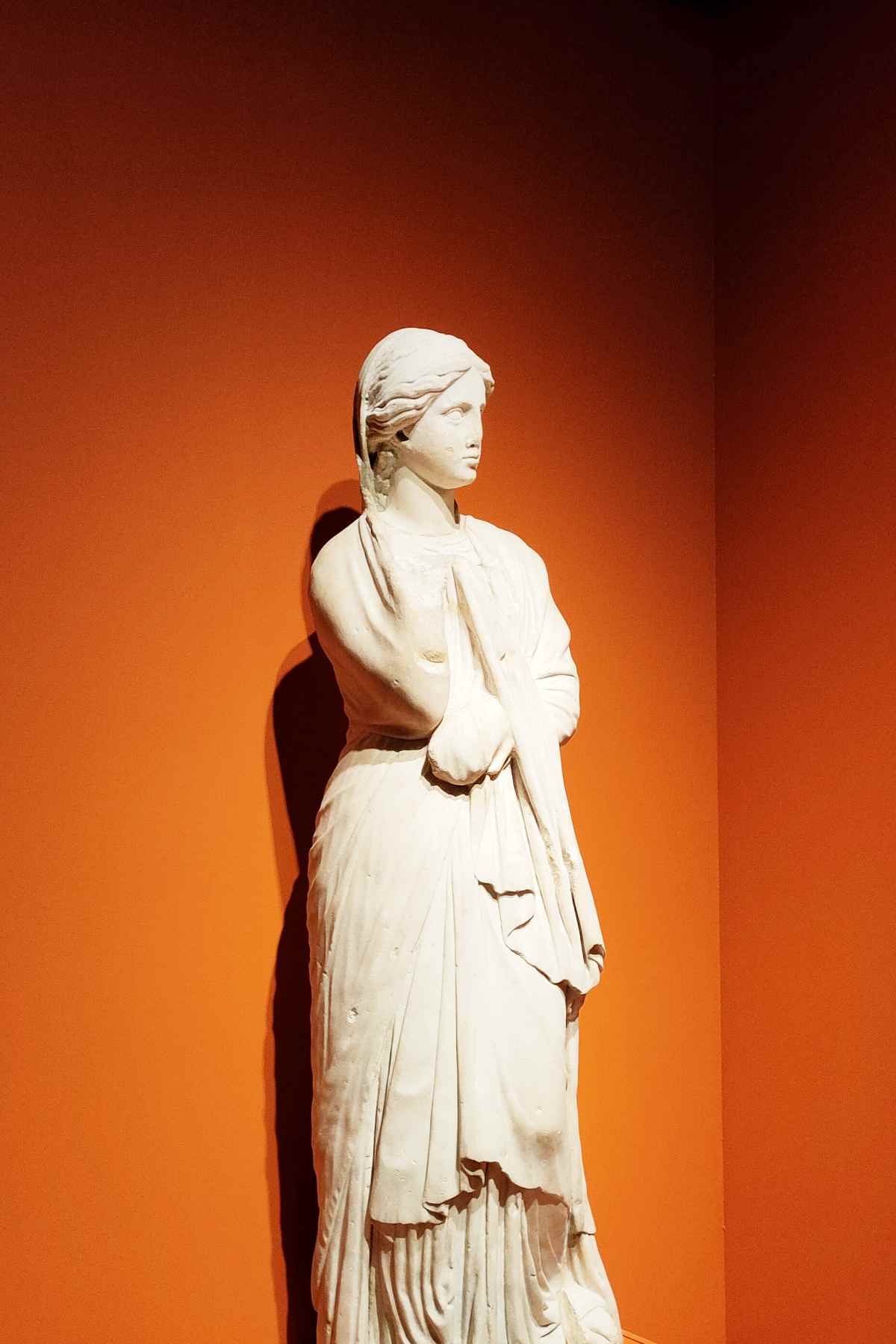 Greek woman statue in front of an orange wall.