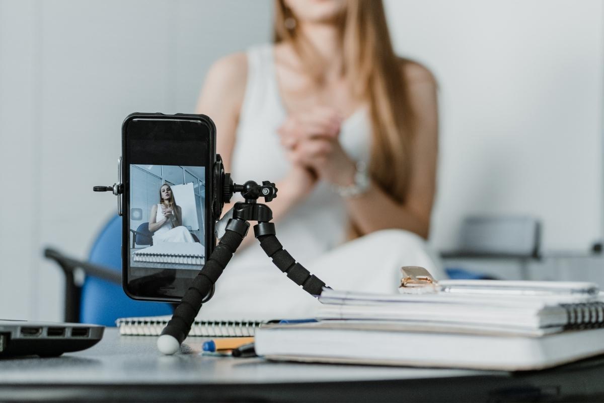 Phone on a desk focused on a woman recording a video in the background.