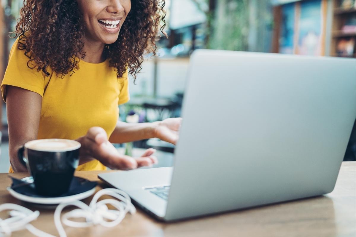 Woman in a yellow shirt behind a laptop. There's a black mug to her right.
