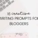 Flatlay of a desk with laptop and notebook, low opacity. 16 creative writing prompts for bloggers is written on the top in black.