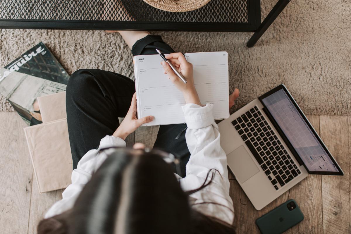 Birds eye view of a woman sitting on the floor, pen in hand, posed over a notebook that's on her knee.