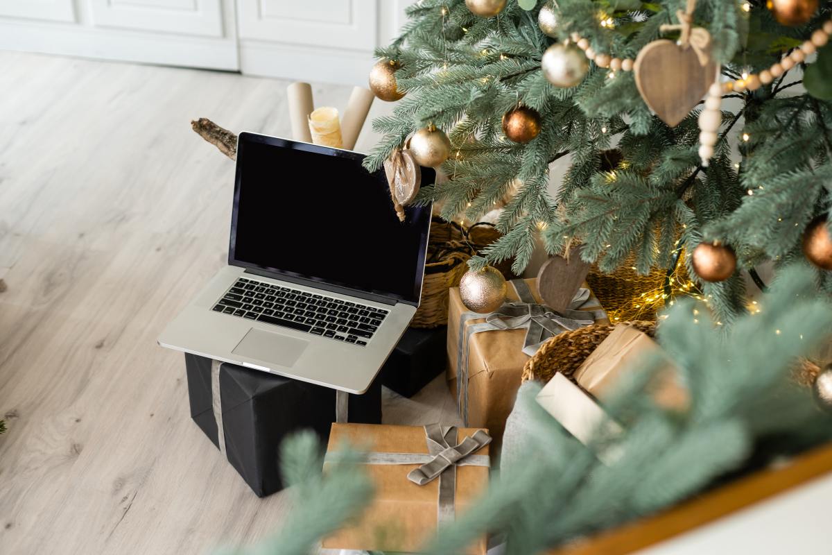 Laptop sitting under a Christmas tree, surrounded by presents.