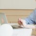 Woman in a blueshirt leaning on a white table with laptop open.
