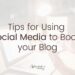 Low opacity image of a woman holding a phone, hovering over a laptop. 'Tips for Using Social Media to Boost your Blog' written in black on top.
