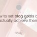 Pinkish hue of a table with notebook and coffee cup on it, with the words 'How to set blog goals and actually achieve them' on top.